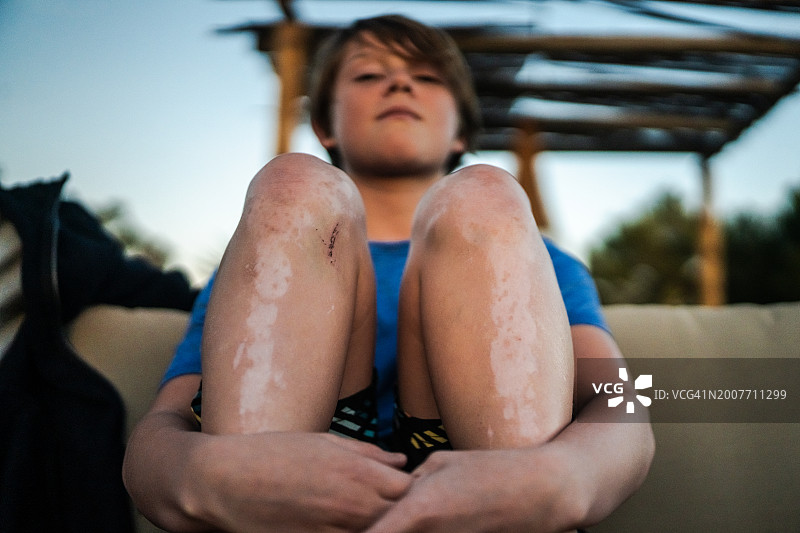 男孩在黄昏时坐在沙发上抱着膝盖图片素材