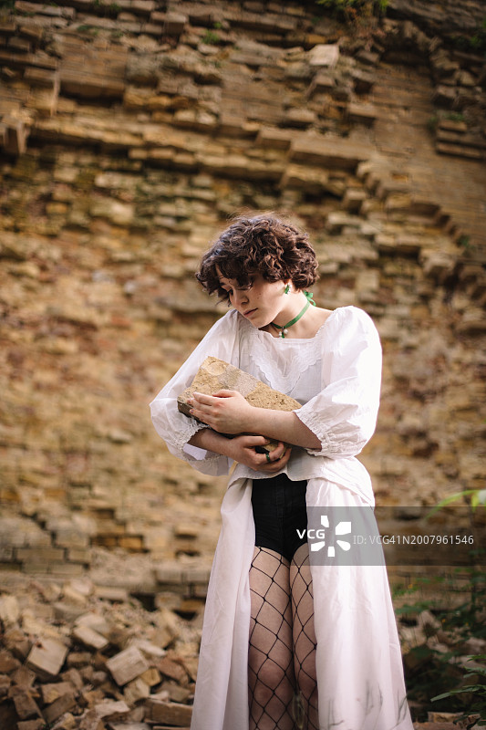 站在破旧砖墙旁的年轻女人拿着砖头图片素材