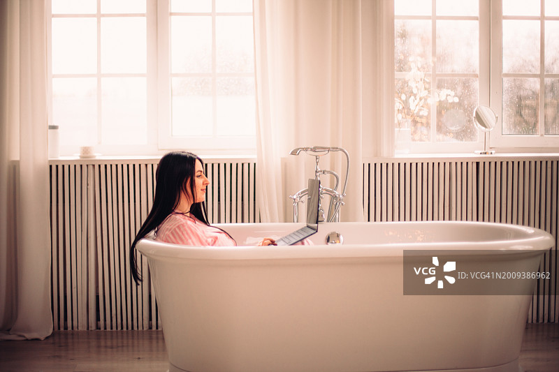 年轻女商人用笔记本电脑在浴缸里工作图片素材