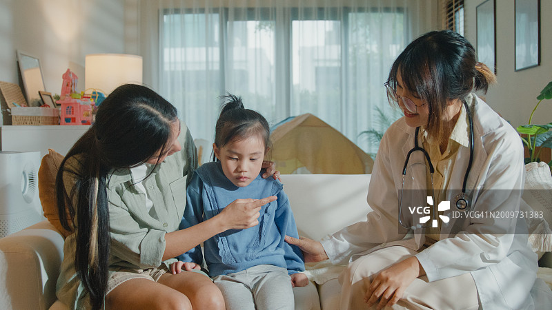 女医生在家中为发烧生病的女孩检查并提供建议，关注患病女孩与母亲的家庭健康图片素材