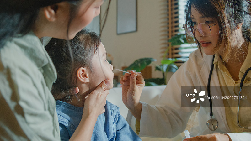 生病发高烧的亚洲女孩在家接受医生鼻拭子检测图片素材