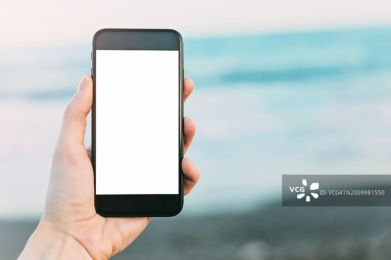 手持智能手机在海滩上显示空白屏幕图片素材