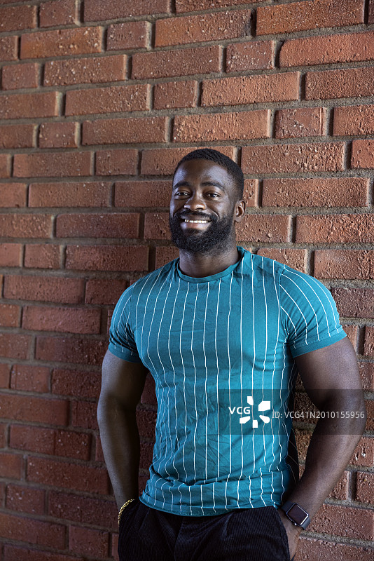 站在砖墙前，双手插在口袋里的微笑男人肖像图片素材