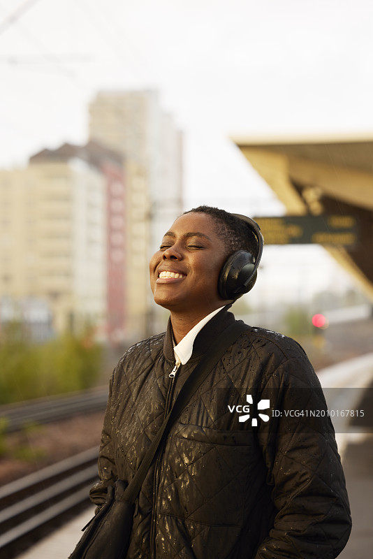 在车站，戴着无线耳机闭着眼睛听音乐的微笑女商人图片素材