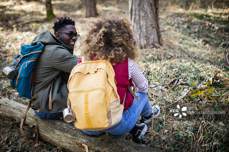 坐在森林圆木上交谈的年轻背包情侣背影图片素材