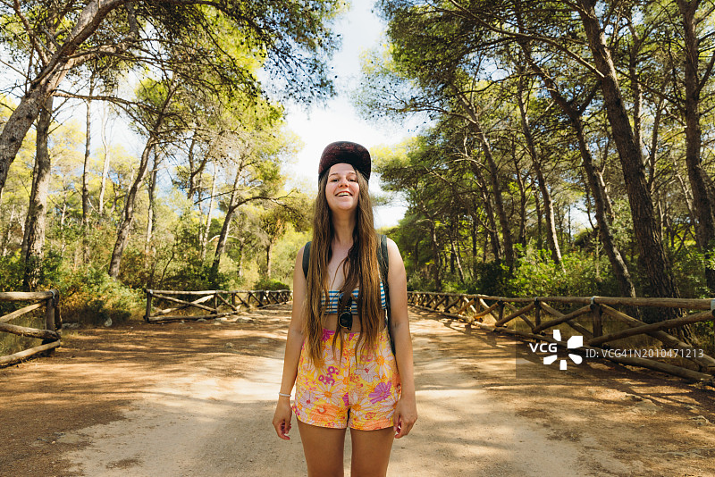 快乐的女子背着背包在意大利普利亚波托塞尔瓦乔国家公园的风景优美的森林中行走图片素材