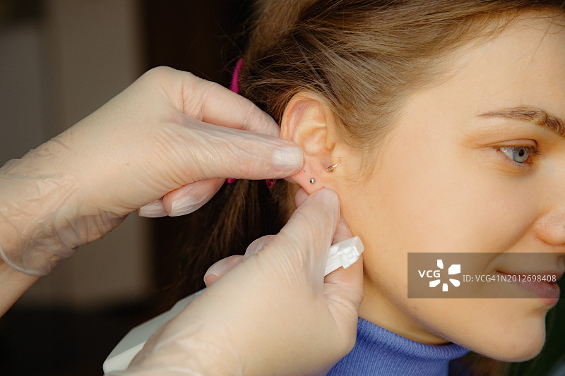 手持穿孔枪的专业人士展示手术结果 - 在满意顾客的耳垂上发光的精致珠宝图片素材