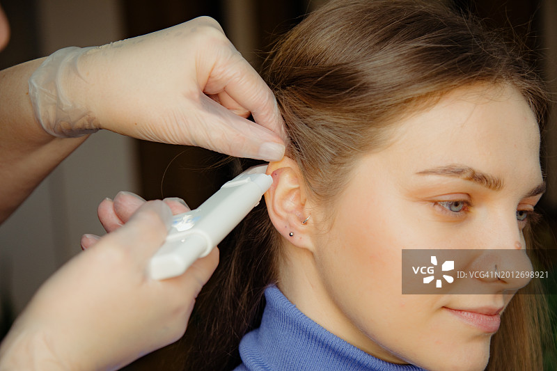 用穿孔枪为客户进行耳软骨穿孔的过程图片素材