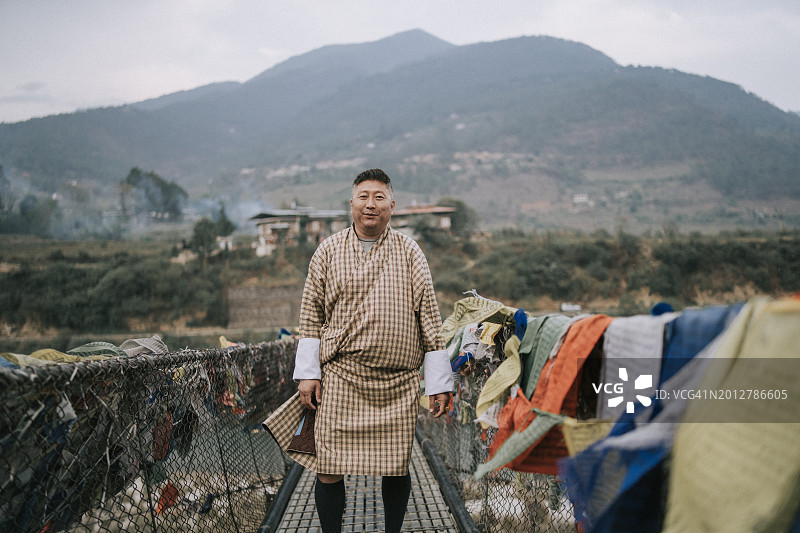 不丹中年男子站在村前桥上，看着镜头图片素材
