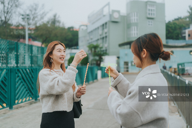 两位年轻的亚洲女性在户外玩耍，她们可能是朋友。左边的人笑着向上看，她们正准备在中国香港玩一些怀旧玩具图片素材