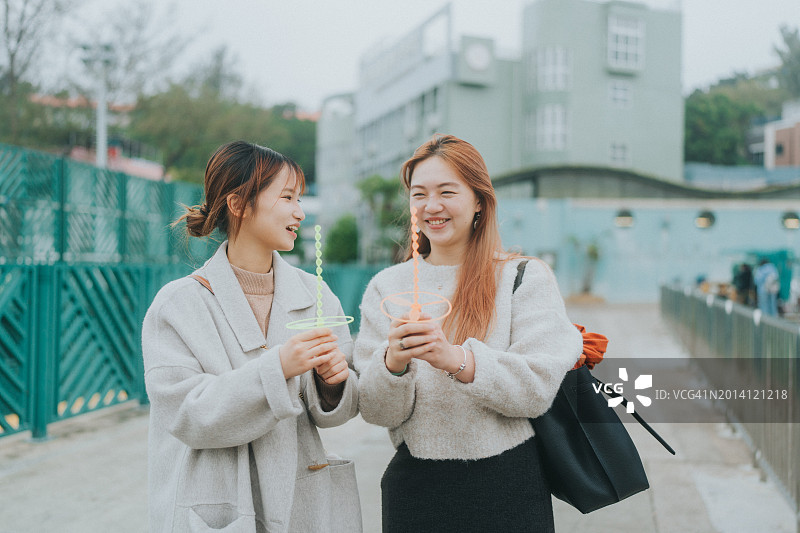 在香港户外散步并愉快交谈，玩着怀旧玩具的两名亚洲年轻女性图片素材