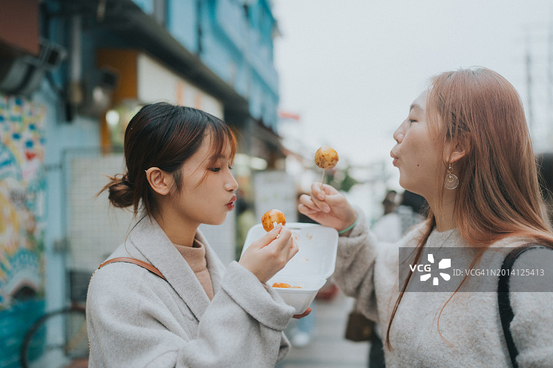 两名亚洲年轻女性在香港户外一起享用街头小吃图片素材