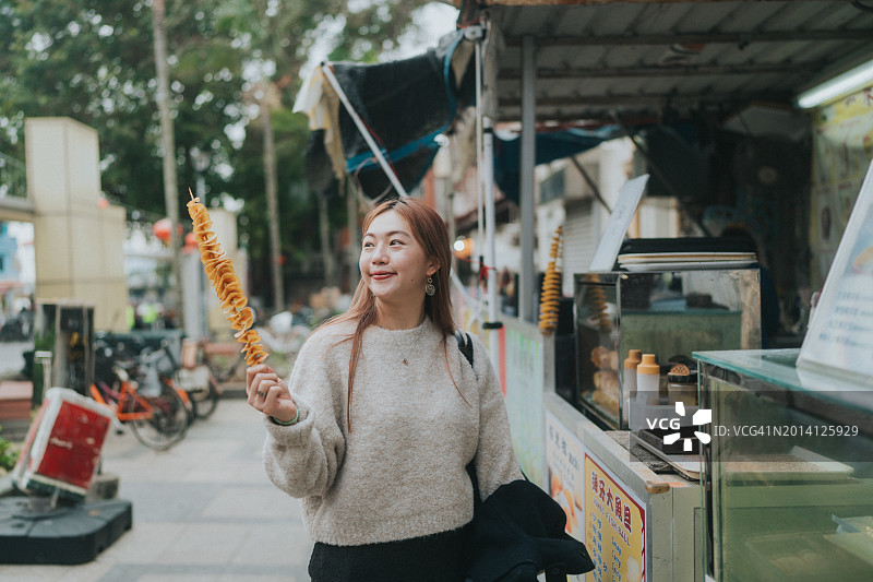 亚洲女性在城市街道上手持螺旋炸薯条图片素材