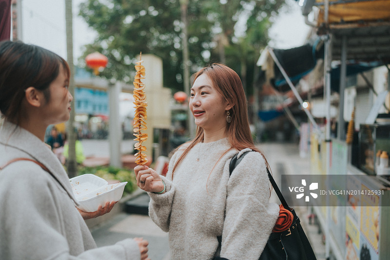 亚洲女性在城市街道上手持螺旋炸薯条图片素材