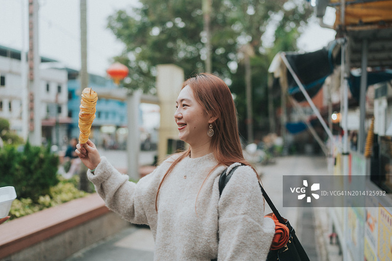 亚洲女性在城市街道上手持螺旋炸薯条图片素材
