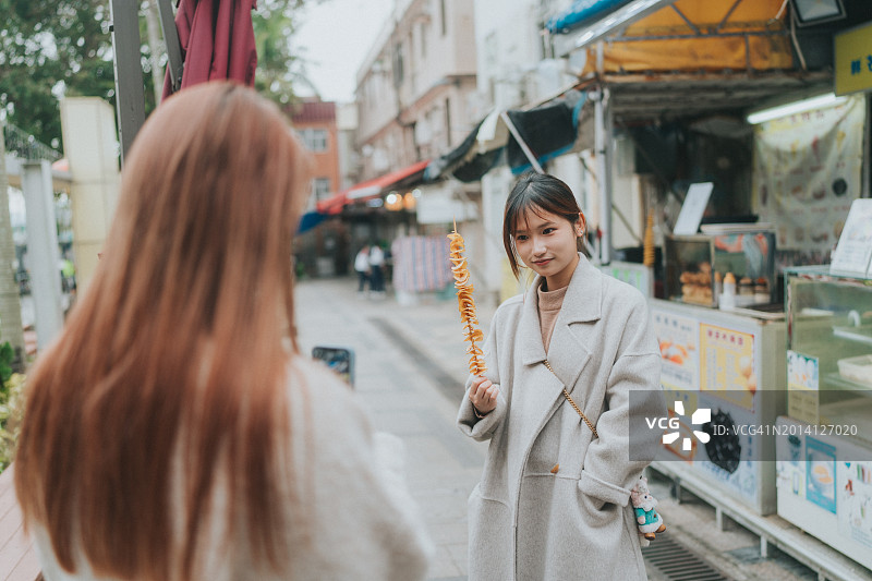 两位亚洲年轻女性微笑合影，其中一位拿着螺旋炸土豆图片素材