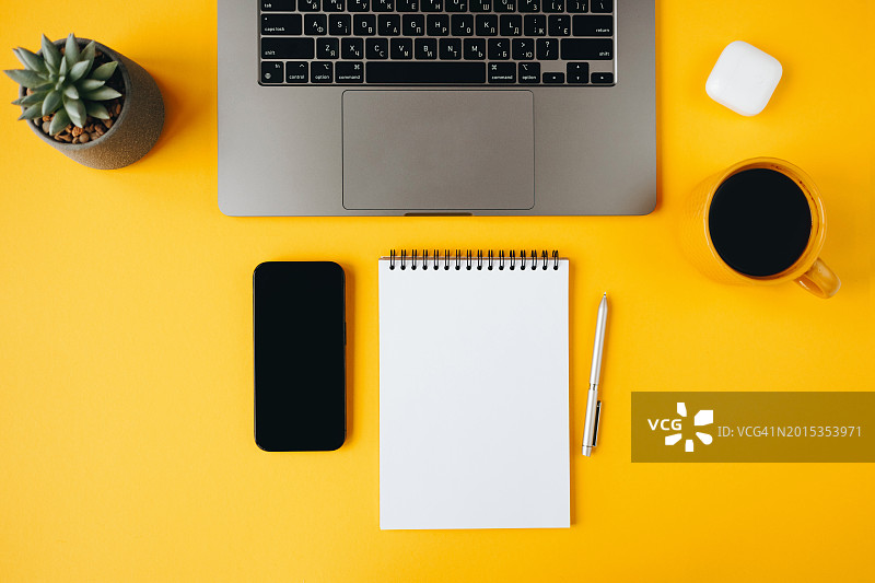 黄色办公桌，带空白笔记本电脑、智能手机和用品图片素材