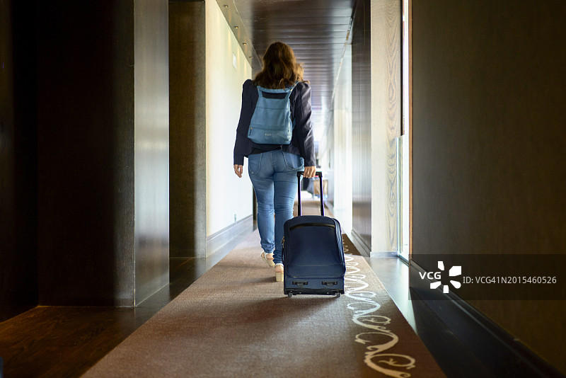 女人在酒店走廊里拉着行李箱的特写，后视图图片素材