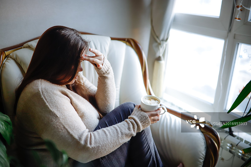 喝咖啡沉思：坐在窗边的加大码毛衣女人头痛不适图片素材