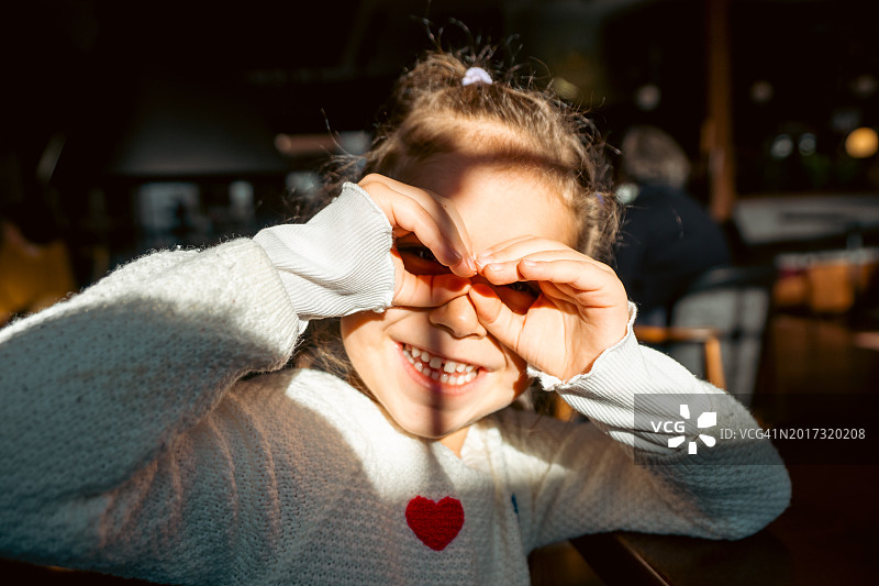 阳光下用想象中的双筒望远镜看东西的微笑小女孩照片图片素材