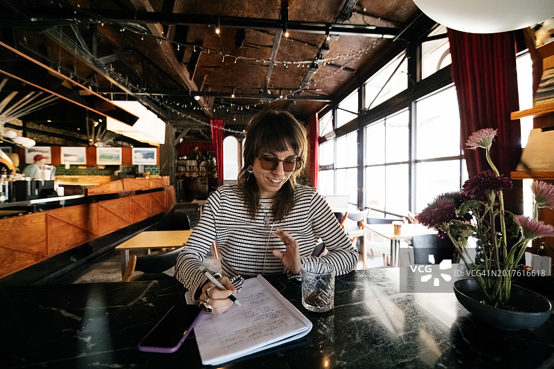年轻女人在咖啡馆工作时在笔记本上写作图片素材