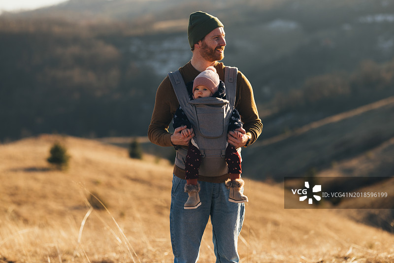慈爱的父亲戴着无檐小便帽，带着婴儿在户外散步图片素材