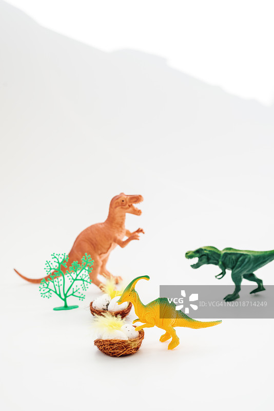 白色背景上靠近带有鸡蛋的巢穴的玩具恐龙图片素材