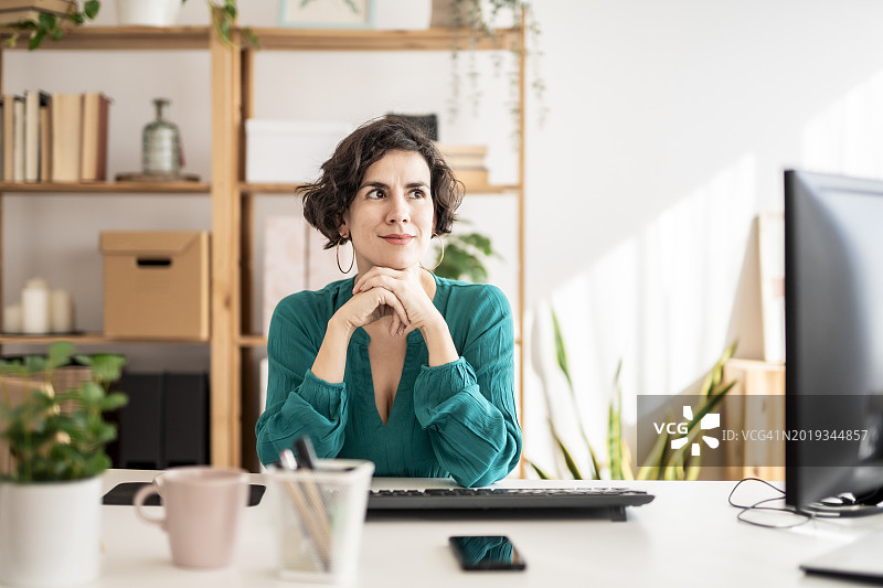 富有创意的女子在现代办公室的办公桌前抬头沉思图片素材