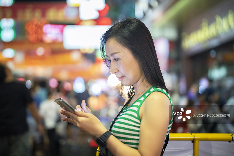 在泰国曼谷夜市步行期间使用智能手机的亚洲女性旅行者图片素材