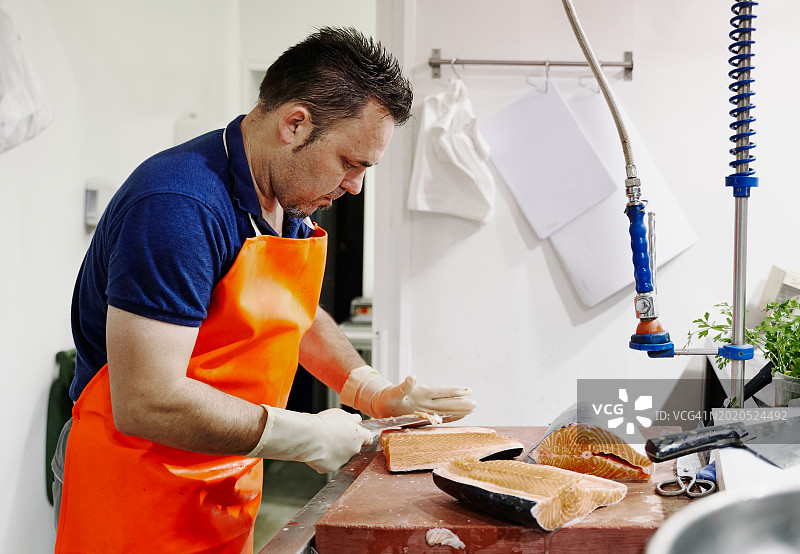 鱼市上，鱼贩戴着橙色围裙正在切三文鱼图片素材