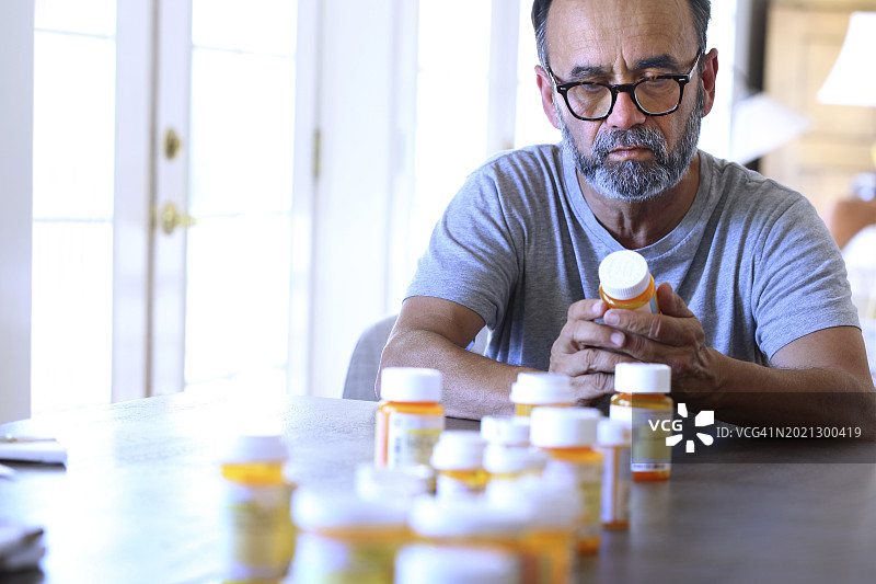 坐在桌旁整理处方药的西班牙裔男人图片素材