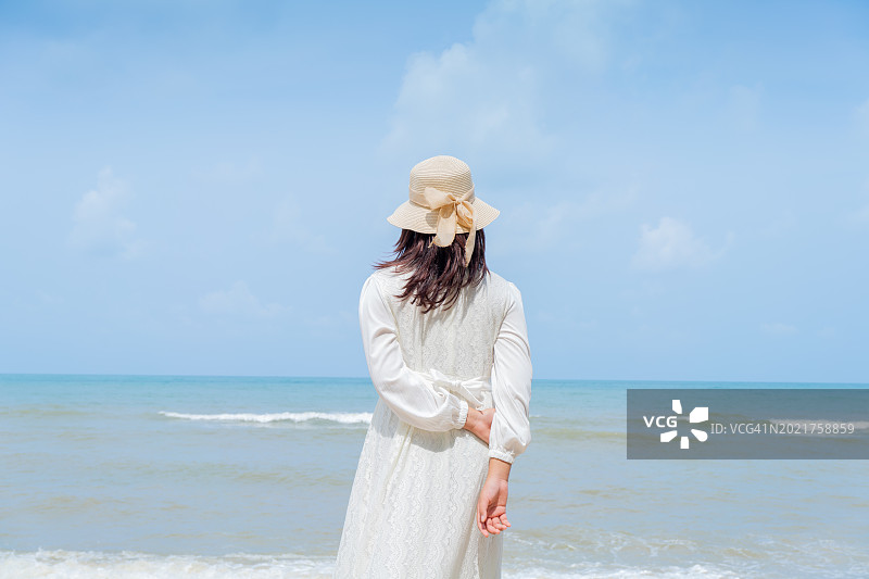 身穿白色连衣裙和帽子的年轻女人站在海滩上，张开双手拥抱大海图片素材