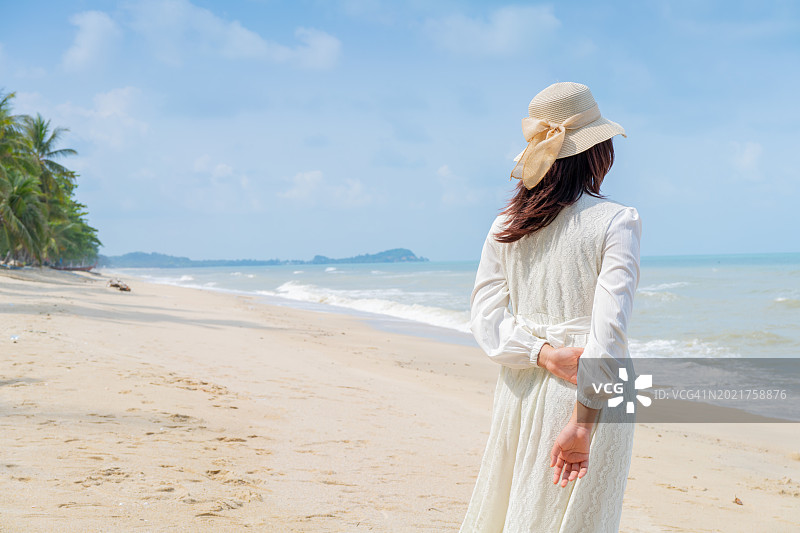 身穿白色连衣裙和帽子的年轻女人站在海滩上，张开双手拥抱大海图片素材