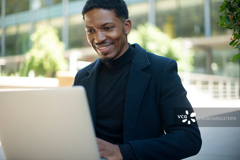 快乐的非洲裔男人在户外使用笔记本电脑进行商务研究和远程工作图片素材