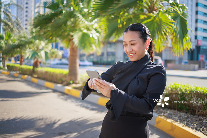 快乐的年轻亚洲女人使用智能手机进行投资，在户外工作图片素材
