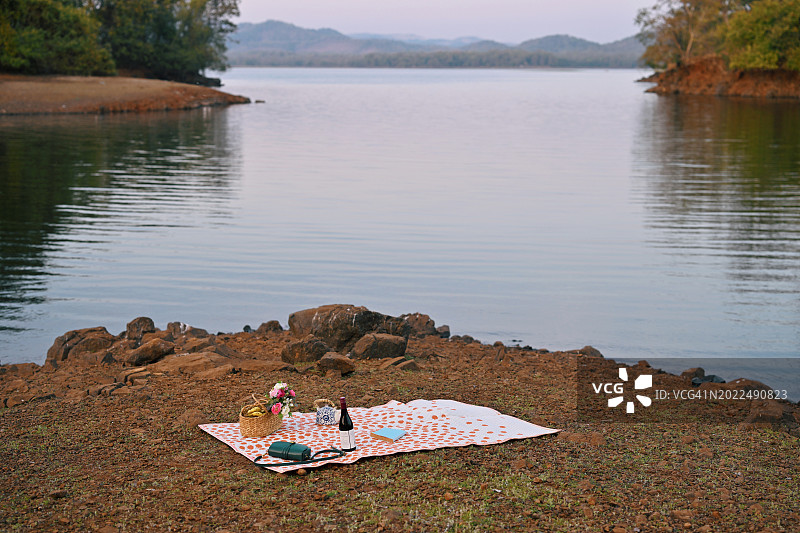 湖边背景下的野餐垫、鲜花水果篮图片素材