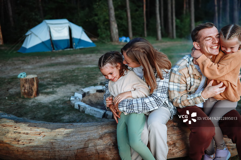 真实的家庭照：父母和两个女儿在森林里拥抱，儿童户外探险图片素材