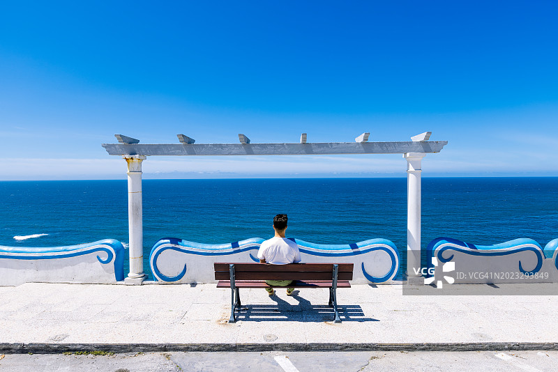男人在晴朗的一天坐在长椅上欣赏海景（葡萄牙埃里塞拉）图片素材