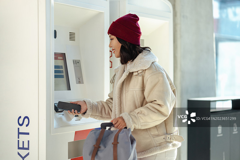 中国亚洲女游客在售票机上购票并用智能手机支付图片素材