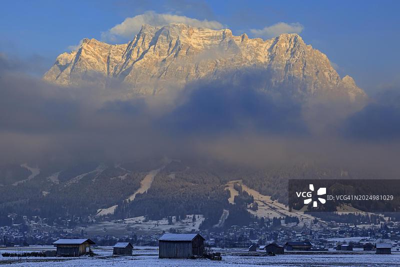 傍晚时分云层之上的陡峭山峰，小屋，冬季，白雪，奥地利蒂罗尔州埃尔瓦尔德和楚格峰图片素材