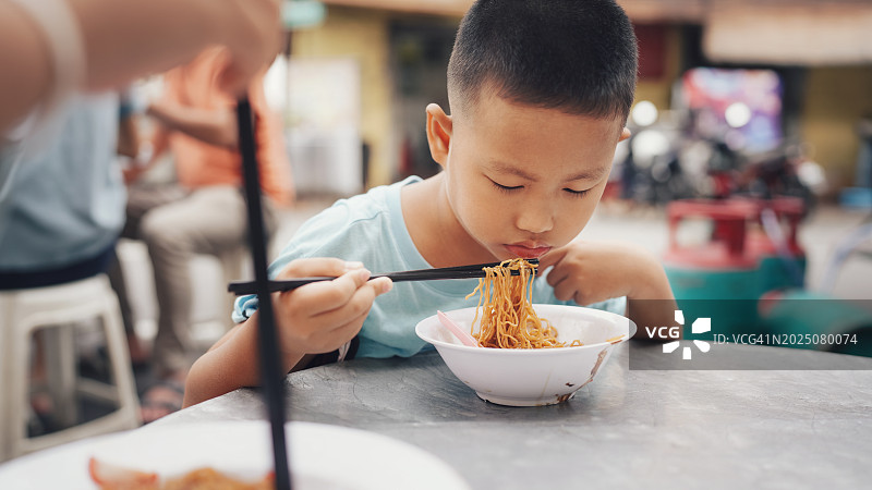 亚洲人在当地街边小摊用筷子吃刚出锅的馄饨面。传统当地饮食文化。槟城著名街头小吃。图片素材