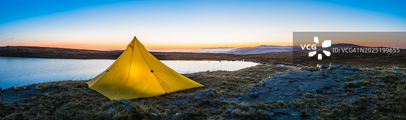 田园诗般的山湖日出时分照亮的黄色帐篷全景图片素材