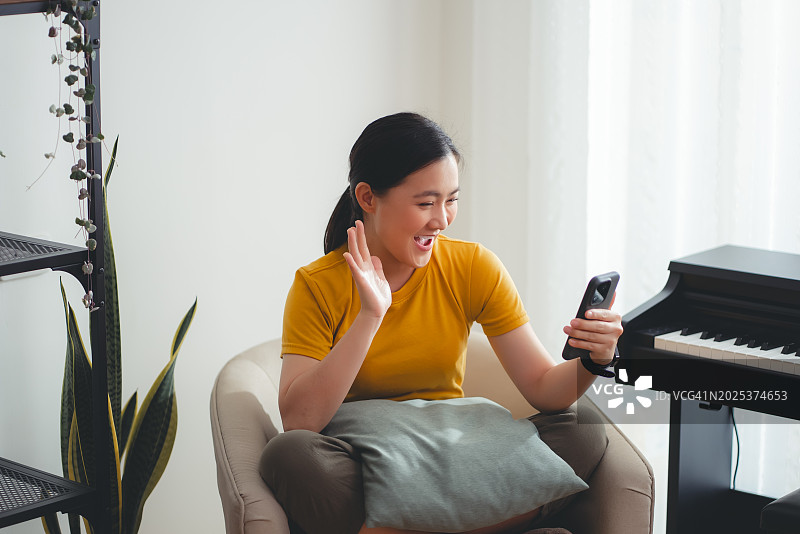 亚洲女人在客厅里用智能手机进行视频通话或直播，笑容满面图片素材
