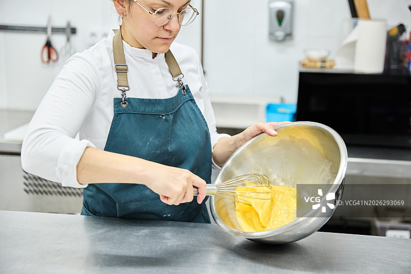 年轻女糕点师在糕点店厨房打鸡蛋制作美味蛋糕图片素材