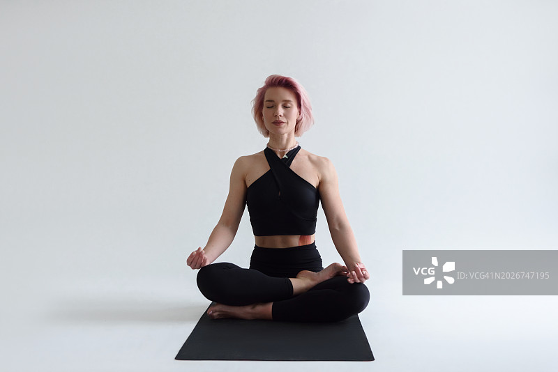 瑜伽：女人在白色背景的垫子上以莲花坐姿冥想图片素材