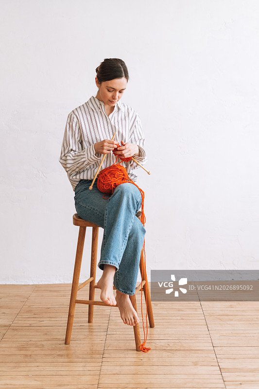 在工作室椅子上用橙色纱线编织的年轻女人肖像图片素材