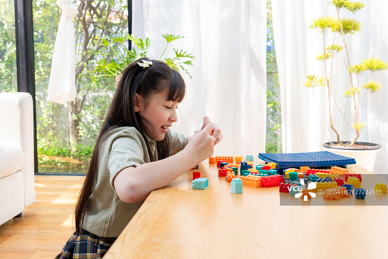 小学生穿着休闲服装坐在舒适的客厅地板上，在周末制作塑料积木人仔，以提高创造力技能的特写镜头。图片素材