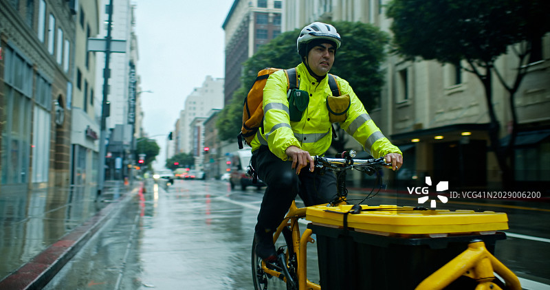 雨天送货员在洛杉矶市中心街道上骑行的中景全身照图片素材