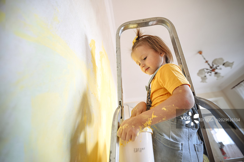 充满活力的DIY：独立女孩在梯子上将房间墙壁漆成黄色图片素材