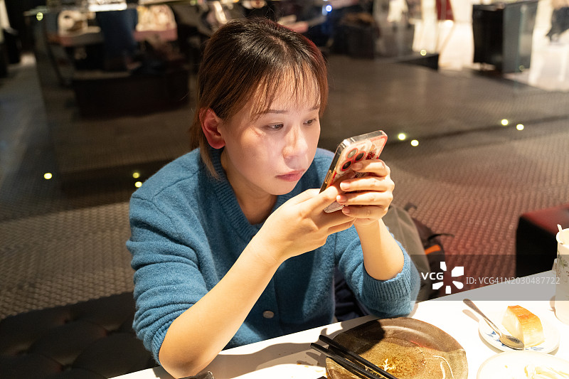 亚洲女性边吃东西边使用手机图片素材